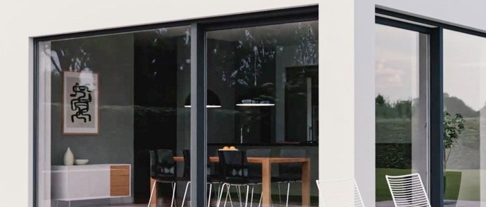 Portefinestre scorrevoli con telaio antracite su facciata bianca, dietro i vetri sala da pranzo con tavolo in legno e sedie nere